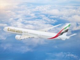 Emirates passenger jet in flight above the clouds tail fin with red green white and black stripes