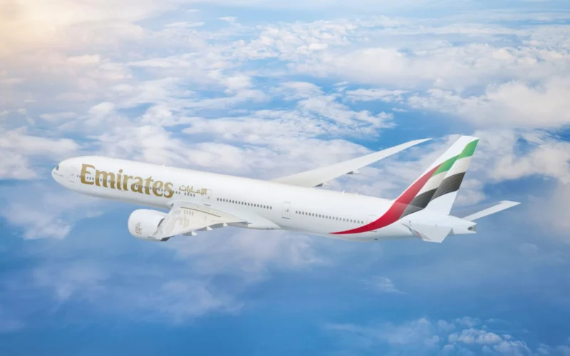Emirates passenger jet in flight above the clouds tail fin with red green white and black stripes