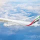 Emirates passenger jet in flight above the clouds tail fin with red green white and black stripes
