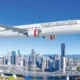 Virgin Australia passenger jet in flight over a city skyline with a river and bridge below against a clear blue sky