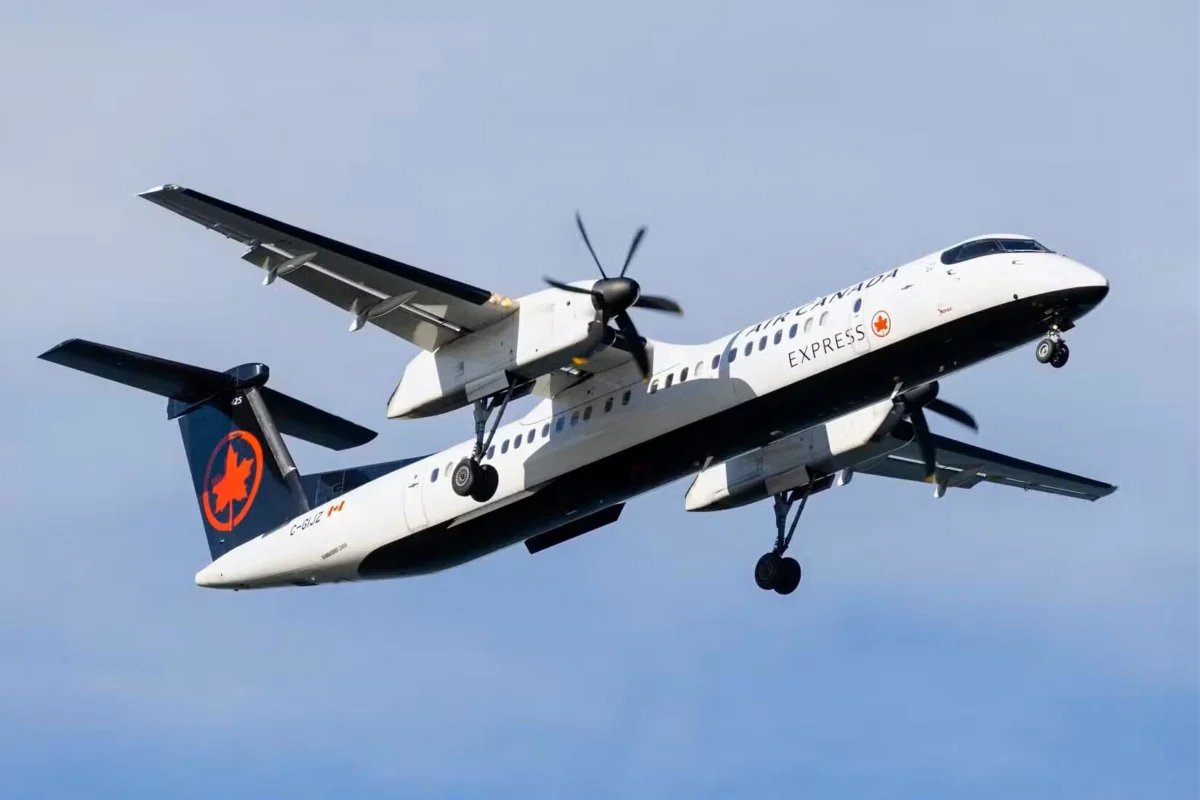 Air Canada Express turboprop in a white and dark blue livery taking off with landing gear down against a blue sky