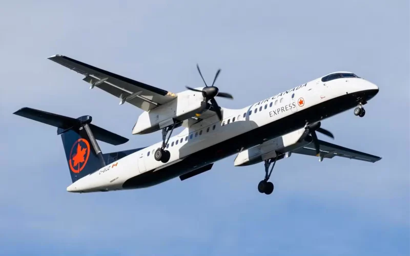 Air Canada Express turboprop in a white and dark blue livery taking off with landing gear down against a blue sky