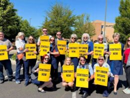 Group of diverse people in a parking lot holding bright yellow signs that read Contract Now and My Union Speaks For Me