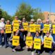 Group of diverse people in a parking lot holding bright yellow signs that read Contract Now and My Union Speaks For Me