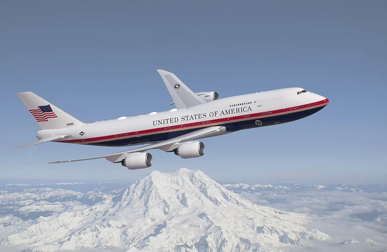 Air Force One presidential aircraft flying over a snow covered mountain range with clear blue sky