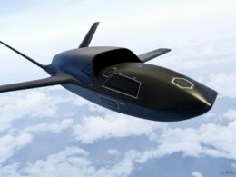 Dark sleek unmanned aircraft with swept back wings flying above clouds in a clear sky