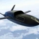 Dark sleek unmanned aircraft with swept back wings flying above clouds in a clear sky