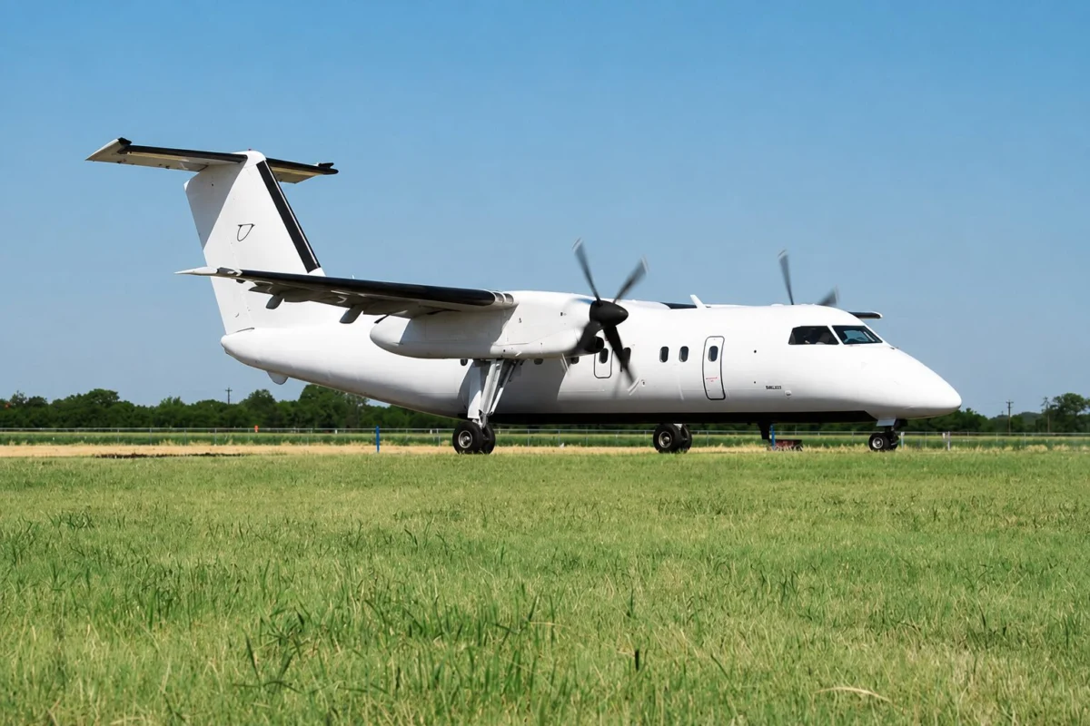berry32 White twinengine turboprop passenger aircraft parked on a grassy airfield with a clear blue sky and a distant tree line