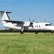 White twinengine turboprop passenger aircraft parked on a grassy airfield with a clear blue sky and a distant tree line