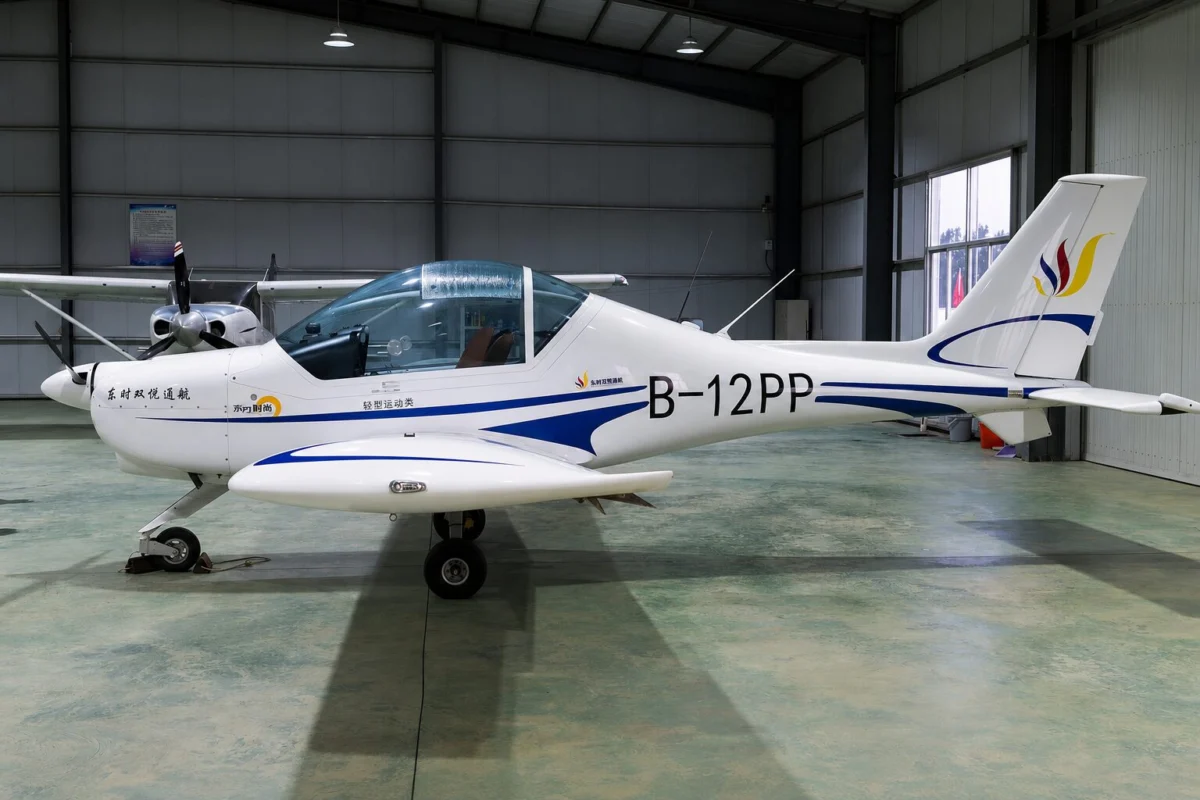 Small white light aircraft with blue accents inside a hangar nose gear down and propeller at left tail marked B 12PP