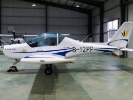 Small white light aircraft with blue accents inside a hangar nose gear down and propeller at left tail marked B 12PP