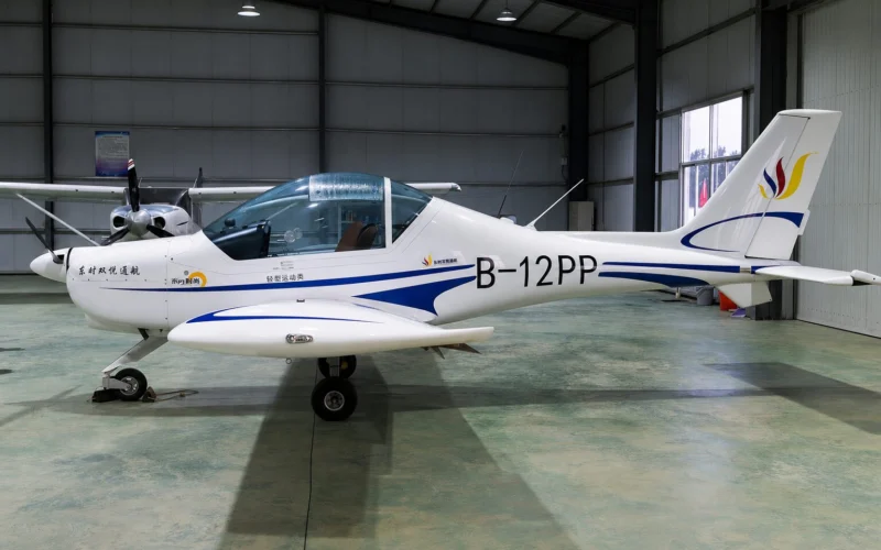 Small white light aircraft with blue accents inside a hangar nose gear down and propeller at left tail marked B 12PP