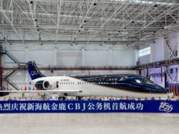 Inside a spacious hangar a dark blue and white private jet sits behind a long blue banner with Chinese text and a row of people posing in front