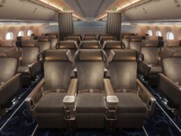 Interior of an airplane cabin with rows of brown leather seats armrests and windows along the sides