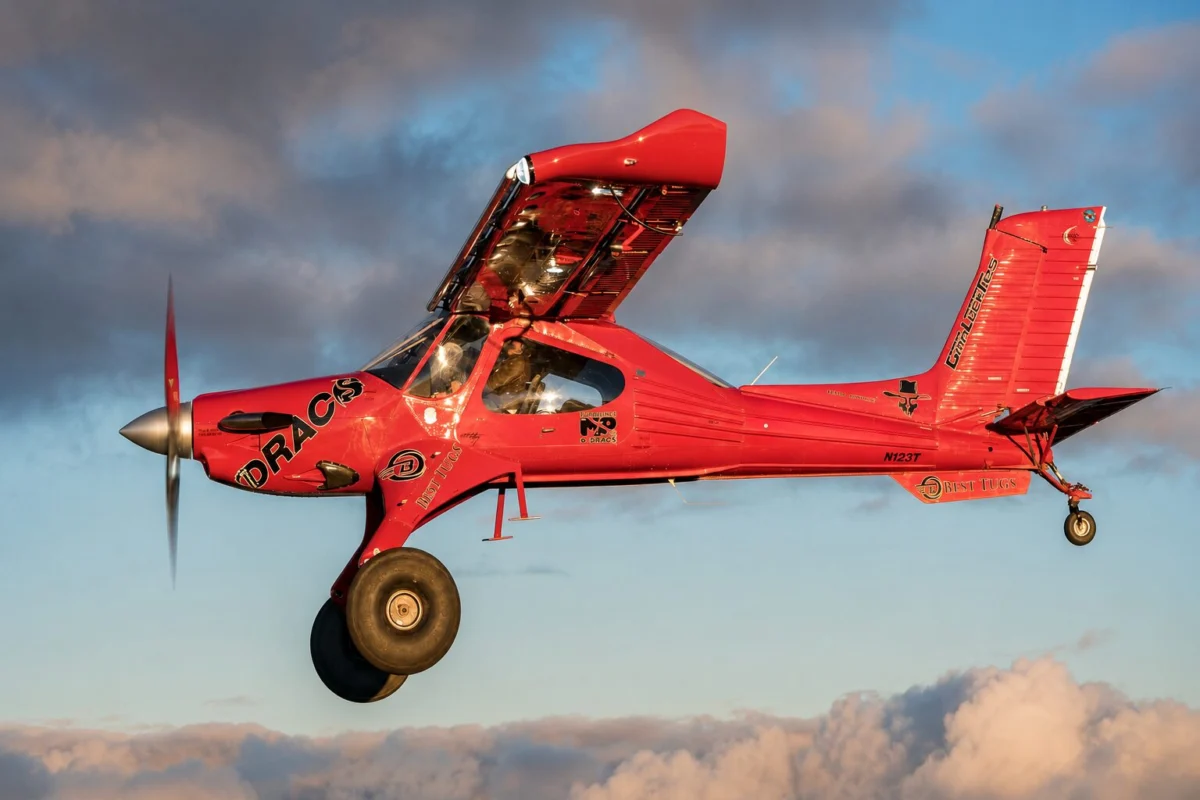 Red aerobatic airplane in midflight propeller blurred blue sky with clouds in the background showcasing its branding on the fuselage