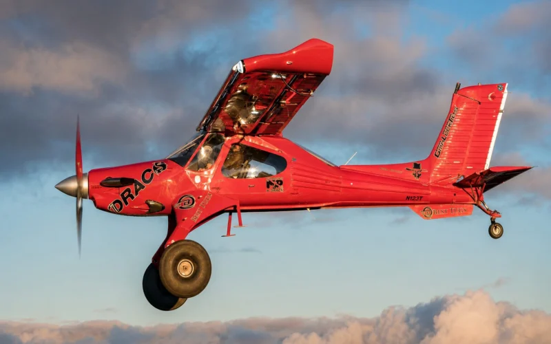 Red aerobatic airplane in midflight propeller blurred blue sky with clouds in the background showcasing its branding on the fuselage