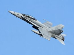 Twin seat military fighter jet banking to the left against a clear blue sky cockpit canopy visible with two pilots inside