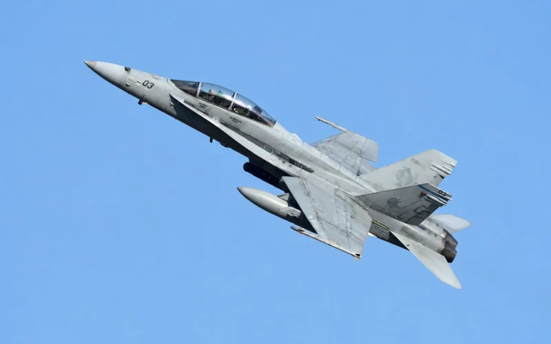 Twin seat military fighter jet banking to the left against a clear blue sky cockpit canopy visible with two pilots inside