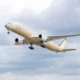 Beige passenger jet with red wingtip climbs into a cloudy sky during takeoff landing gear down