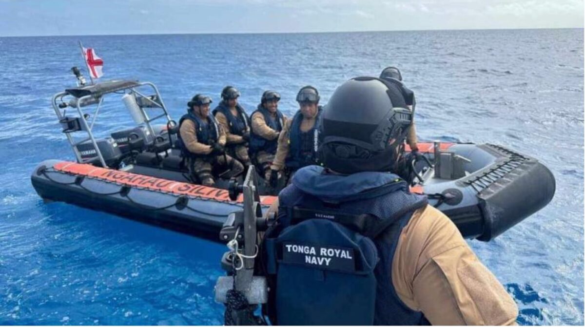 image Tonga Royal Navy crew in tan uniforms sit in a black inflatable rescue boat at sea with a responder in the foreground wearing navy gear