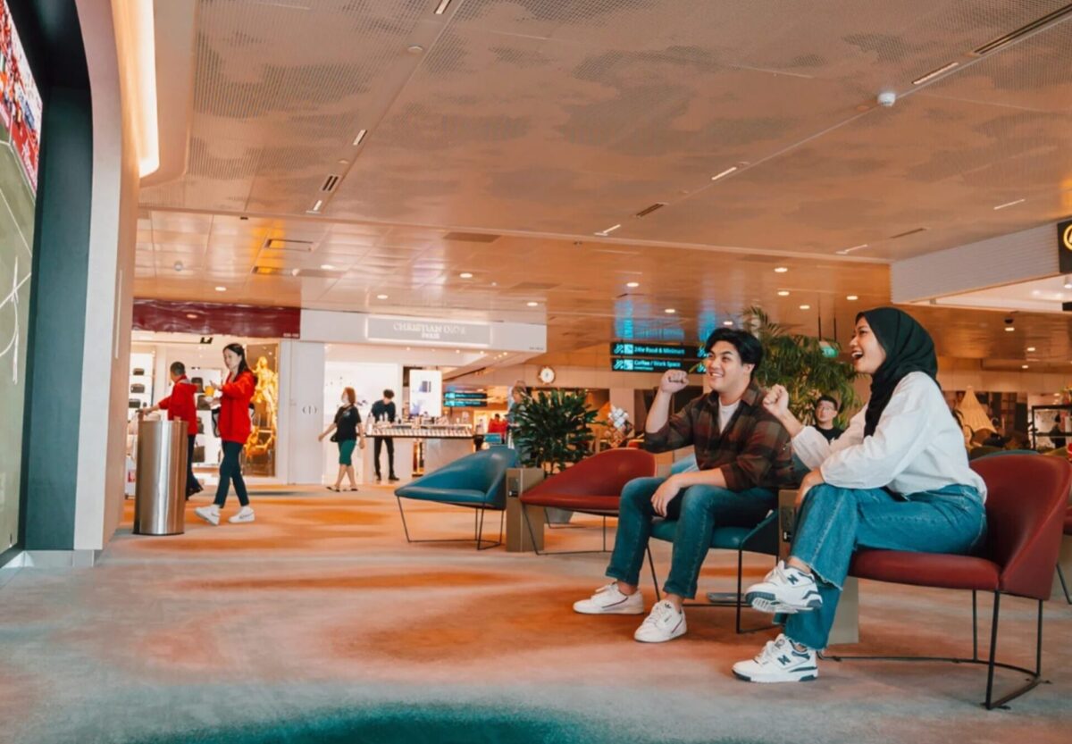 image Two friends sit on red chairs in a mall lounge smiling and cheering