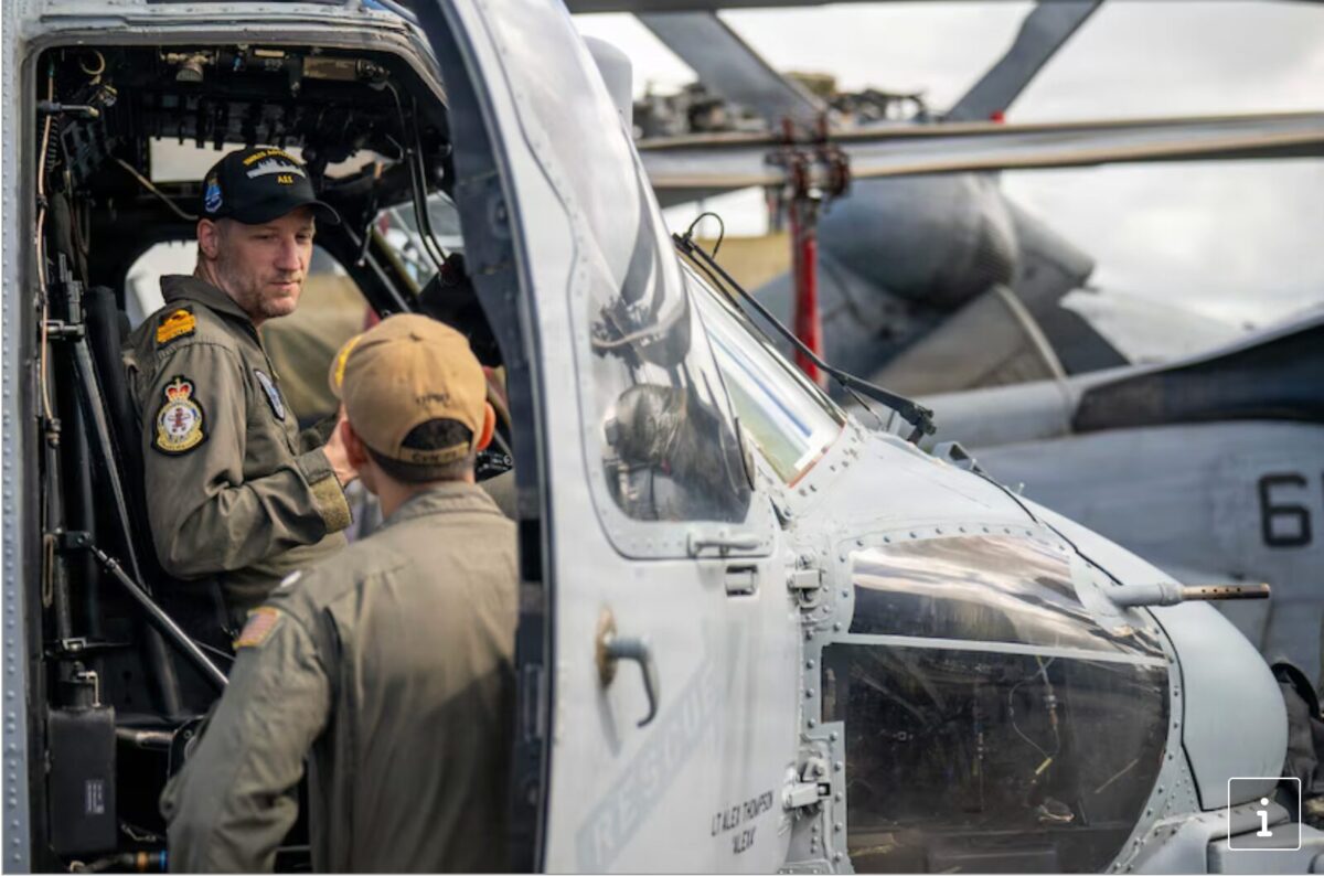 image Two pilots in green flight suits sit in a helicopter cockpit preparing for departure