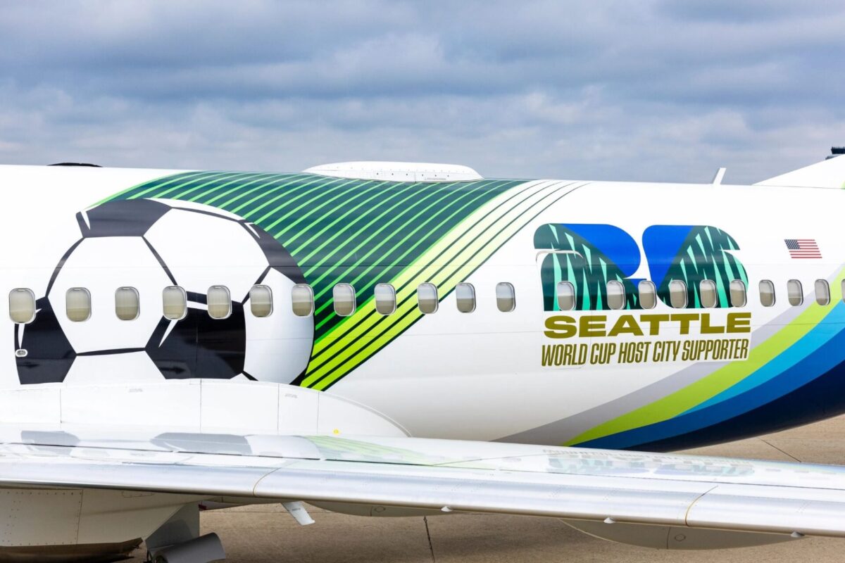 image Side view of a commercial jet featuring a large soccer ball graphic and bright greenblue stripes with Seattle World Cup Host City Sponsor branding and a small US flag nearby