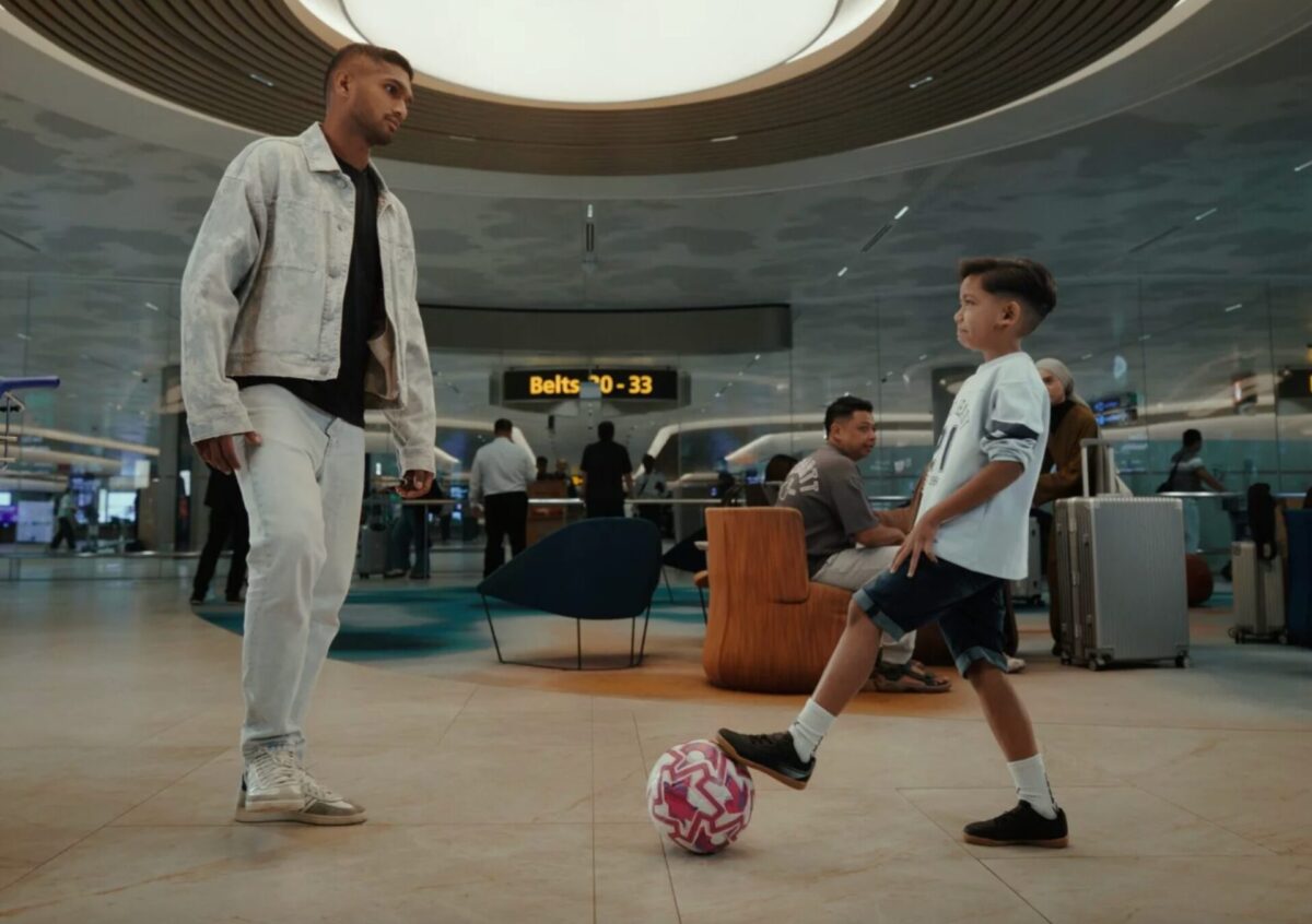 image Boy kicks a colorful soccer ball in an airport terminal while a man watches nearby