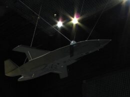 Unmanned aerial vehicle gray flying wing drone suspended by cables inside an anechoic test chamber at a sound testing facility