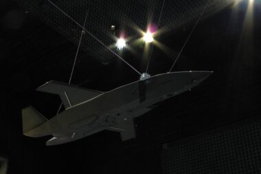 Unmanned aerial vehicle gray flying wing drone suspended by cables inside an anechoic test chamber at a sound testing facility