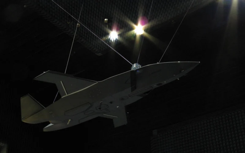 Unmanned aerial vehicle gray flying wing drone suspended by cables inside an anechoic test chamber at a sound testing facility