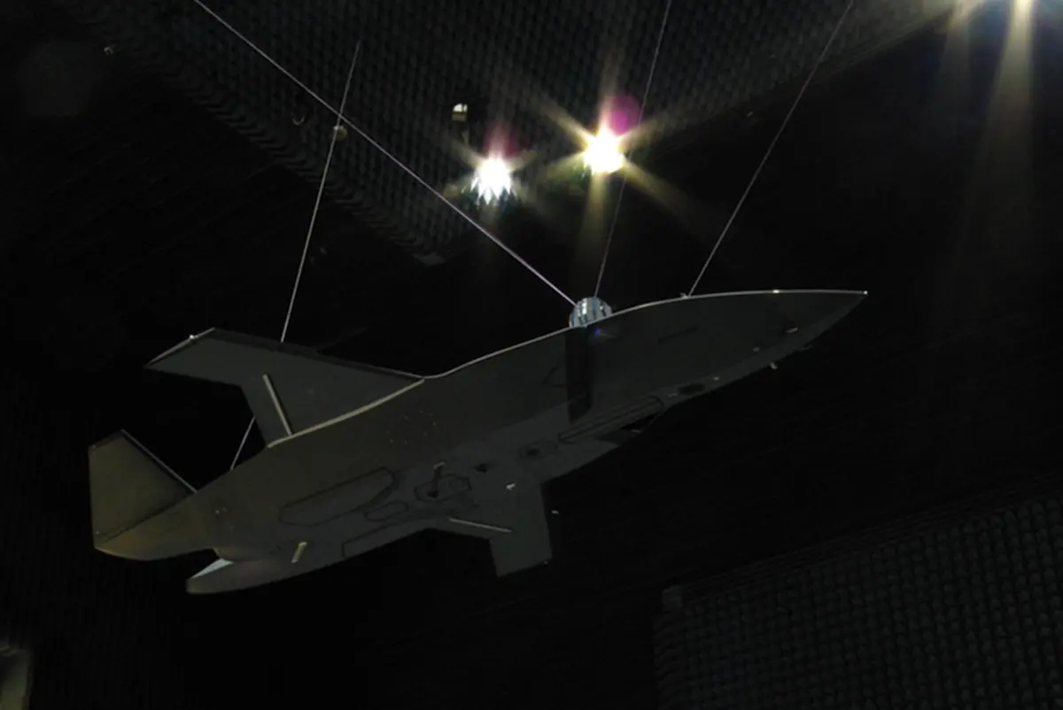 mq28hires Unmanned aerial vehicle gray flying wing drone suspended by cables inside an anechoic test chamber at a sound testing facility