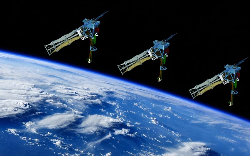 Three blue satellite like structures with extended robotic arms float above Earths curved horizon in space against black sky