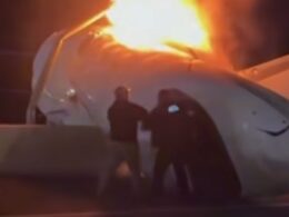Airplane fuselage on fire with bright flames silhouettes of responders at a nighttime crash site
