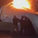 Airplane fuselage on fire with bright flames silhouettes of responders at a nighttime crash site
