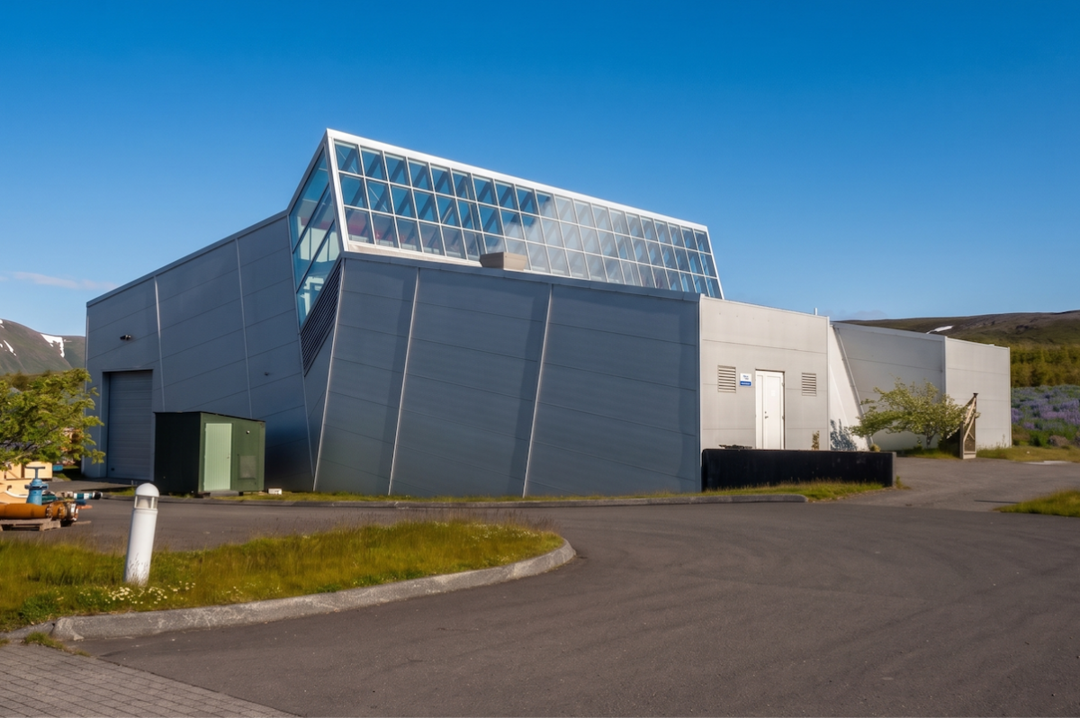 syntholene plant iceland Modern industrial building with sloped gray walls and a glass roofed upper section against a blue sky