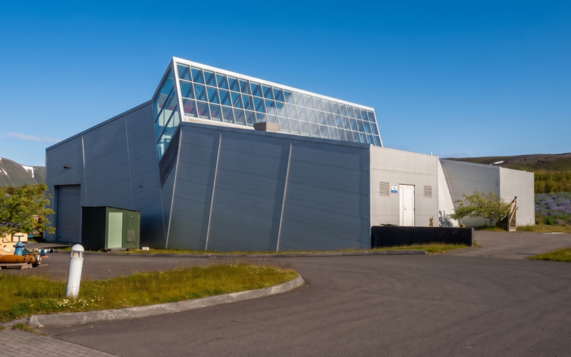 syntholene plant iceland Modern industrial building with sloped gray walls and a glass roofed upper section against a blue sky