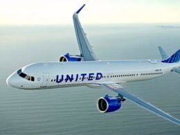 Side view of a United Airlines passenger jet flying over the ocean white fuselage with blue United lettering and blue engine nacelles