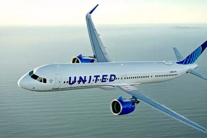 Side view of a United Airlines passenger jet flying over the ocean white fuselage with blue United lettering and blue engine nacelles