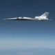 NASA X 59 QueSST experimental aircraft in white with a long pointed nose flying high above a blue sky and distant mountains