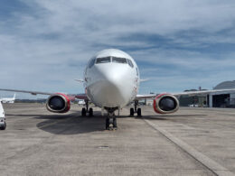 Front view of a white passenger jet on taxiway with red engine nacelles and ground equipment nearby