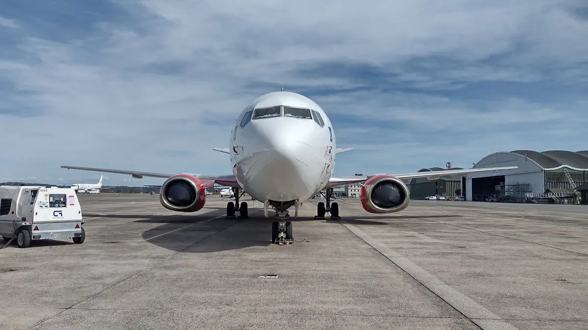 001 2 Front view of a white passenger jet on taxiway with red engine nacelles and ground equipment nearby