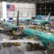 Interior of an aircraft manufacturing hangar with multiple teal colored jetliners on the assembly line and yellow maintenance platforms surrounding them