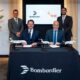 Two men seated at a signing table signing documents as two others stand behind them jet models on the table Bombardier branding and flowers in the background