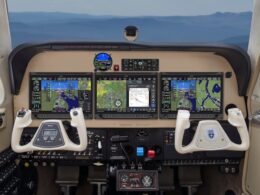 Modern airplane cockpit with four widescreen flight displays dual control yokes and cockpit controls visible below the screens