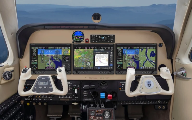Modern airplane cockpit with four widescreen flight displays dual control yokes and cockpit controls visible below the screens