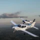 Two white singleengine airplanes in formation midflight over a green valley with a winding river and distant hills at sunsetdusk N204DR visible