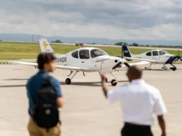 Two white Cirrus airplanes on an airport tarmac with blurred spectators in the foreground and a cloudy sky above