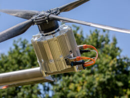 Close up of a carbon fiber rotor hub with a silver finned power electronics unit and orange cables outdoors