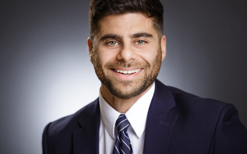 AJ Abedin Avia Solutions Group Professional headshot of a smiling man in a navy suit and striped tie against a neutral gradient background